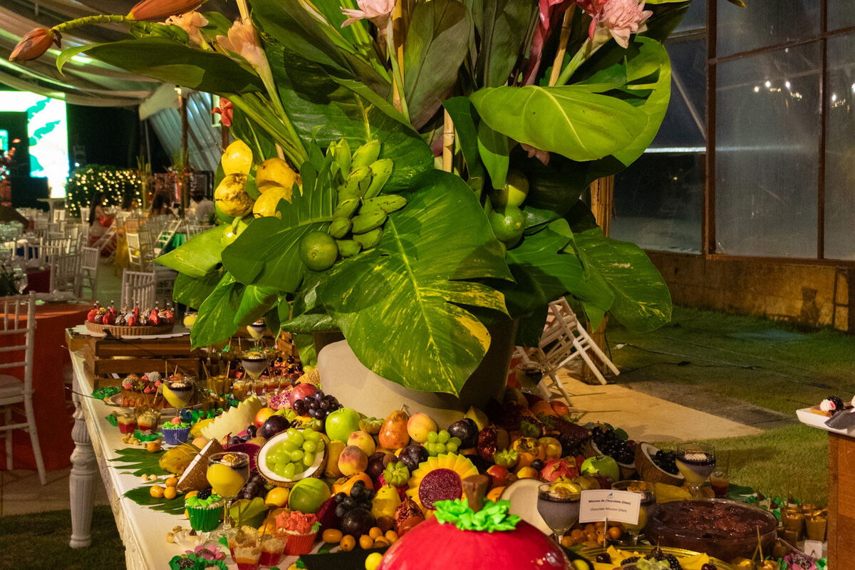 Buffet montado à noite, com grande arranjo de folhagem e frutas sobre a mesa.